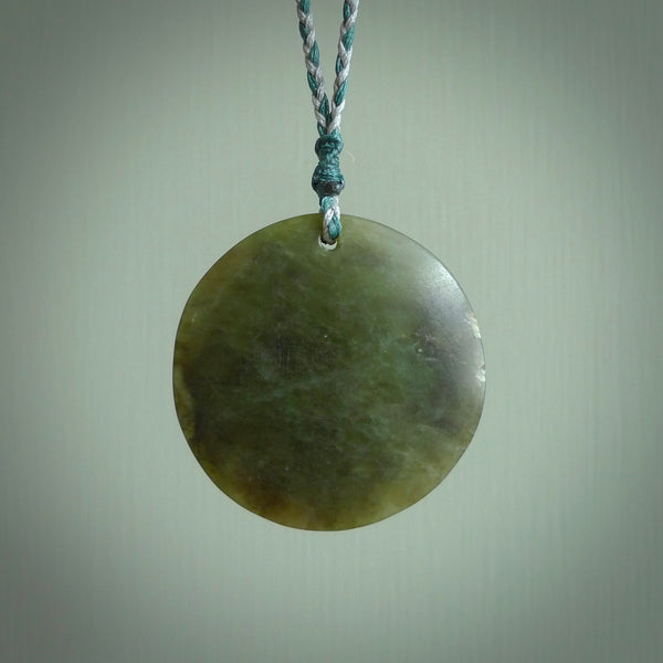 Hand carved jade disc pendant. One side has a double koru etched into the face. This is a subtle and beautiful design. The other side is plain. The cord is a tan colour and is adjustable. The piece was carved for NZ Pacific by Rueben Tipene.