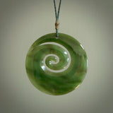 This picture shows a large hand-carved koru. It is carved from British Columbian jade and is suspended from a hand-plaited, black cord. Free delivery worldwide. BC Jade koru necklace.
