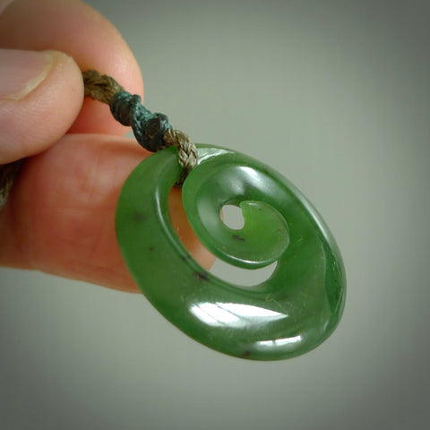 Hand carved New Zealand jade koru pendant. Delivered to you on a hand plaited manuka green cord which is adjustable. Free delivery worldwide.
