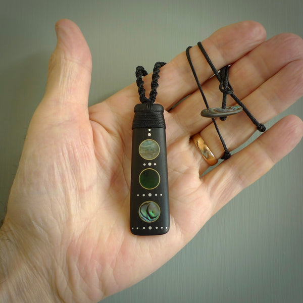 This photo shows a medium sized Toki pendant hand carved from lignum vitae with Afghani Lapis Lazuli and American Turquoise, Paua Shell inlay alongside; brass and silver. This is a stand out one off necklace for those who appreciate art to wear. It is provided with a cord in brown that is a fixed length with Paua Shell Toggle. We ship this piece worldwide and shipping is included in the price.