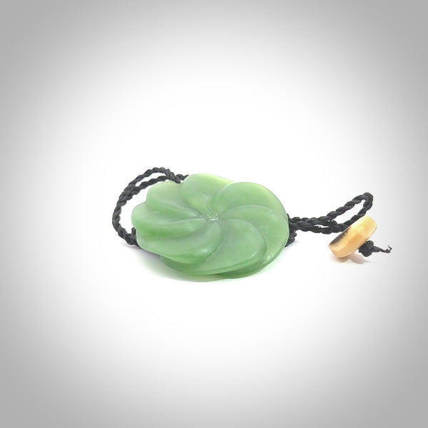 A large and beautiful hand carved 8 fold flower pendant. This piece is carved from New Zealand jade by Jeromy Van Riel. This is a wonderful large toki bound with a hand-plaited cord and a traditional lashing. A beautiful, traditional toki for sale online.