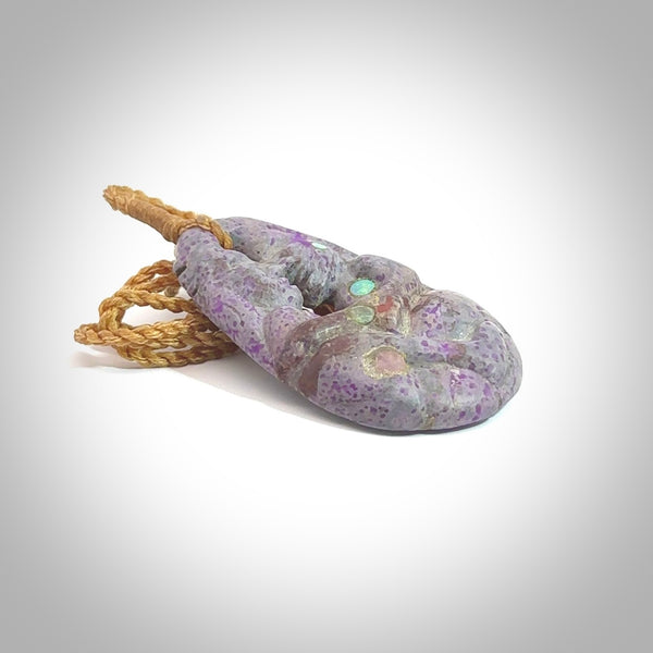 A large and beautiful hand carved partner hoongi pendant in sugilite. This piece is carved from purple Sugilite stone by Jeromy Van Riel with opal and rubys. This is a wonderful work of art to wear and comes with a hand-plaited cord and a bone toggle. A beautiful, unique pendant by Jeromy Van Riel for sale online.