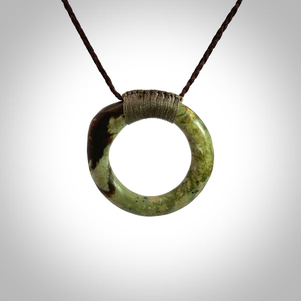 This picture shows a hand carved jade circle pendant with sterling silver inlay. The jade is a very dark green with a shimmer of black tones in the stone. It is suspended from an adjustable Black or Sage coloured cord. Delivery is free worldwide.