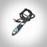 This photo shows a medium sized taiaha pendant hand carved from piano key with Afghani Lapis Lazuli and Chinese Glowing Stone, Sleeping Beauty Turquoise inlay alongside; brass and silver. This is a stand out one off necklace for those who appreciate art to wear. It is provided with a cord in black that is a fixed length with Paua Shell Toggle. We ship this piece worldwide and shipping is included in the price.
