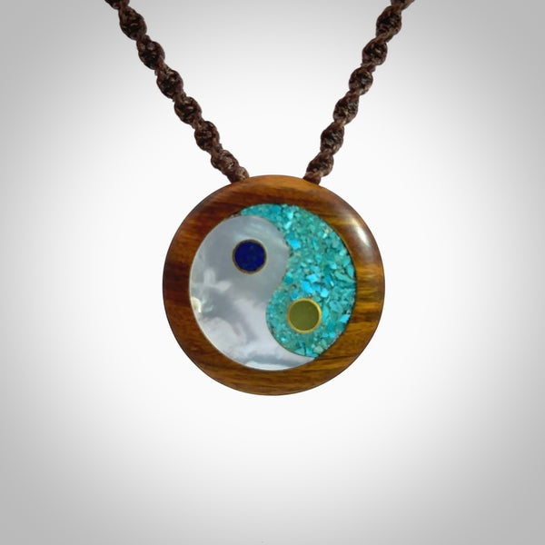 This photo shows a medium sized yin and yang pendant hand carved from lignum vitae with New Zealand Pounamu Jade, Lapis Lazuli, Mother of Pearl and Paua Shell inlay alongside; brass and silver. This is a stand out one off necklace for those who appreciate art to wear. It is provided with a cord in brown that is a fixed length with Paua Shell Toggle. We ship this piece worldwide and shipping is included in the price.
