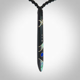 This photo shows a medium sized taiaha pendant hand carved from piano key with Afghani Lapis Lazuli and Chinese Glowing Stone, Sleeping Beauty Turquoise inlay alongside; brass and silver. This is a stand out one off necklace for those who appreciate art to wear. It is provided with a cord in black that is a fixed length with Paua Shell Toggle. We ship this piece worldwide and shipping is included in the price.