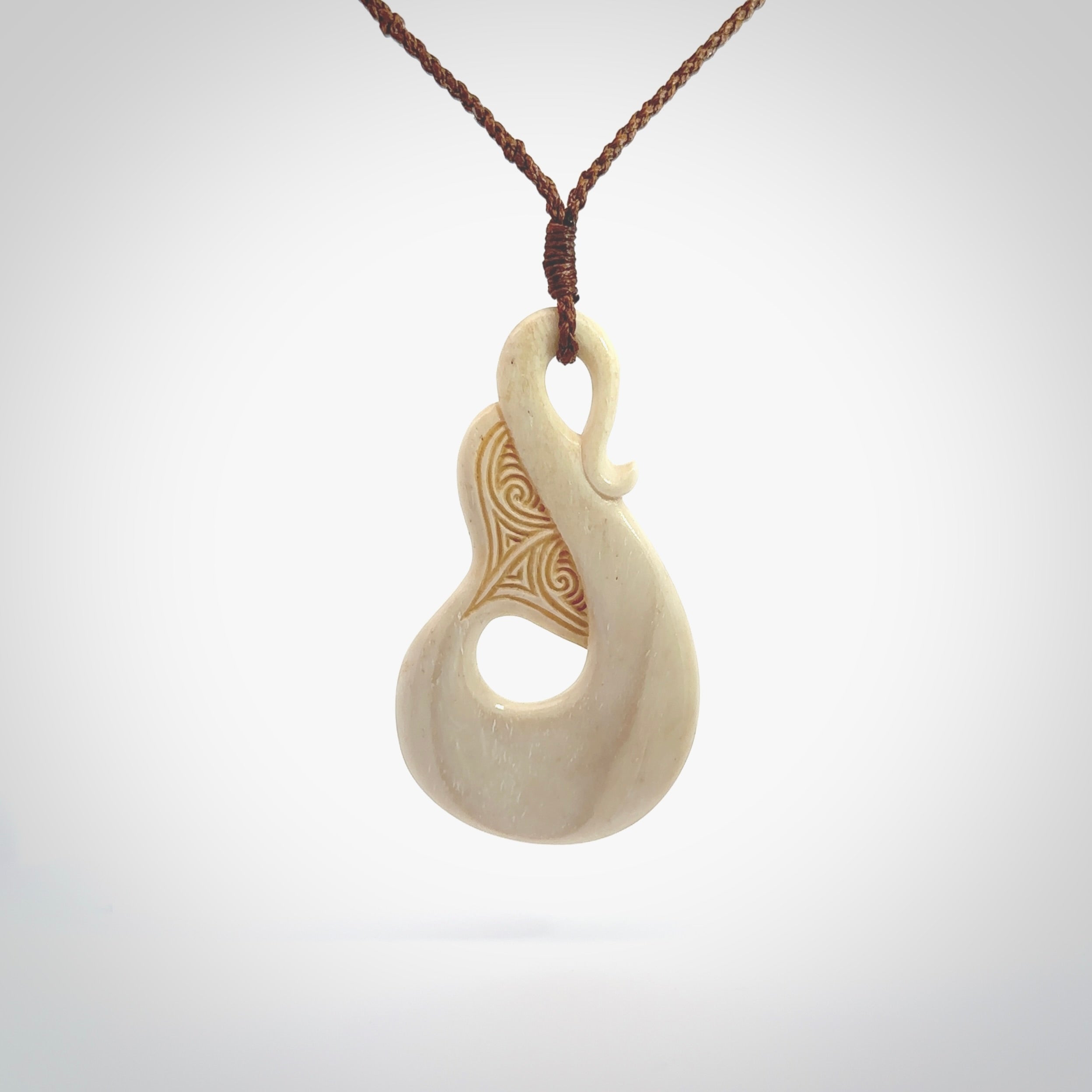 Hand carved Bone Whale Tail pendant with Paua shell inlay by Andrew Doughty. Whale tail pendant by Andrew Doughty with engraving in it. Beautiful unisex necklace hand carved in New Zealand, delivered in a woven kete pouch. Provided with an adjustable brown cord.