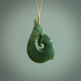 This picture shows a hand carved jade koru pendant. It is a deep green colour and is a wonderful, large sized piece of jewellery. The cord is a four plait beige colour and adjustable so that you can position the pendant where it suits you best. This koru was carved for us by Ric Moor. Delivery is free worldwide.