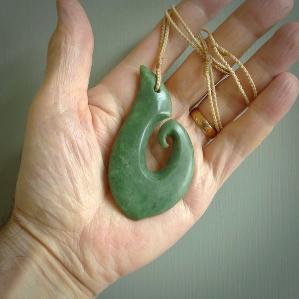 This picture shows a hand carved jade koru pendant. It is a deep green colour and is a wonderful, large sized piece of jewellery. The cord is a four plait beige colour and adjustable so that you can position the pendant where it suits you best. This koru was carved for us by Ric Moor. Delivery is free worldwide.