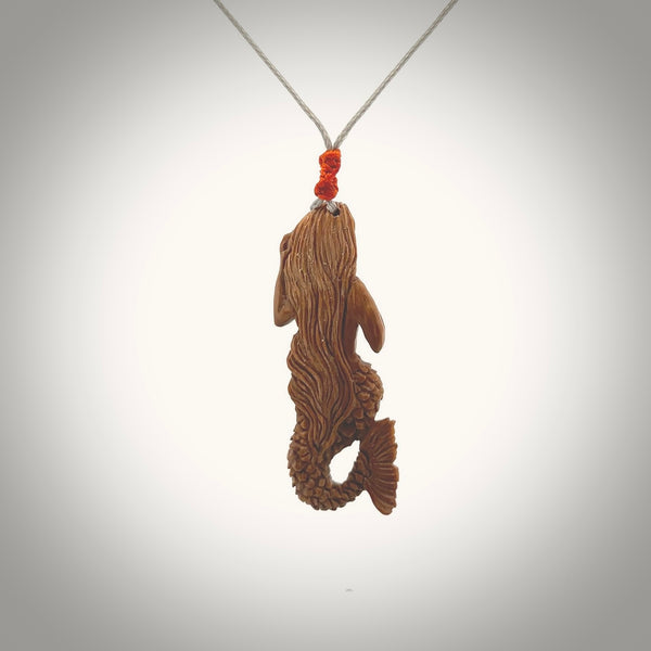 This photo shows a photo of a mermaid pendant. It is handcarved from a beautifully creamy piece of woolly mammoth tusk. It is suspended on an adjustable cord.