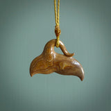 This picture shows a hand carved whale tail pendant. It is a dark, ginger brown colour and is handcarved from Woolly Mammoth tusk. The necklace is made from a braided cord in a mustard colour.