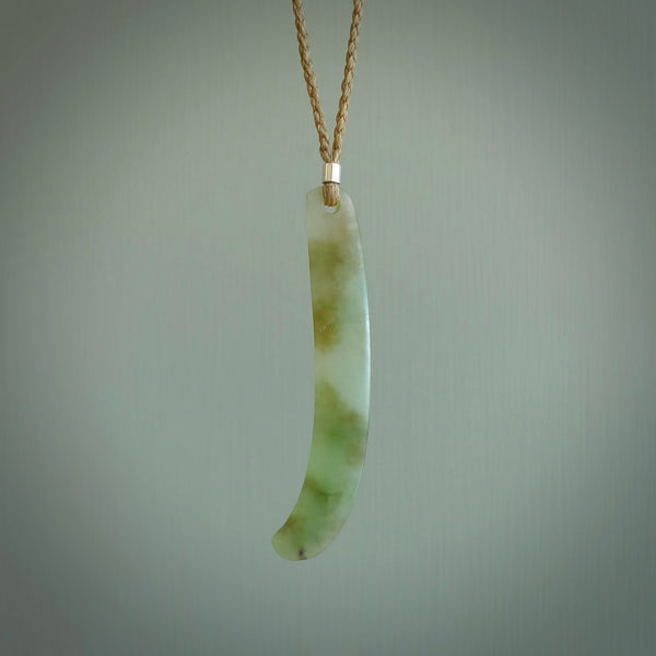This picture shows a hand carved Spoon River White Jade drop pendant with adjustable cord. The jade is a very light, white green with a shimmer of darker tones in the stone. It is suspended from a tan coloured cord. Delivery is free worldwide.