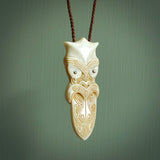 This is a large carved Koruru pendant. It is made from two materials - New Zealand Paua Shell and Bone. The face of the Koruru is carved with a traditional design in the front. It has a protruding tongue which is also carved and the back face has traditional carved designs. This is a large and very traditional pendant that is a collectors piece. This piece is provided on a brown adjustable cord.