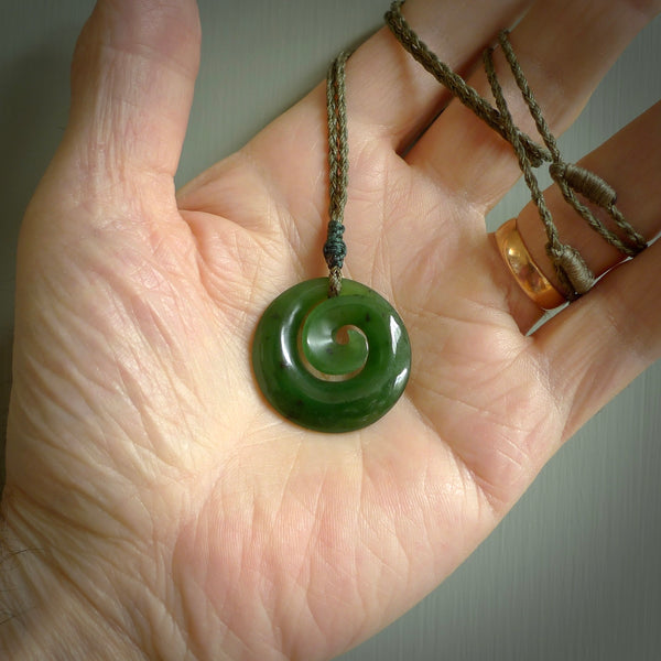 Hand carved New Zealand jade koru pendant. Delivered to you on a hand plaited manuka green cord which is adjustable. Free delivery worldwide.