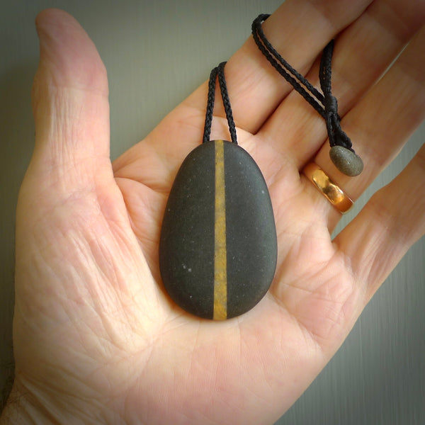Argillite drop pendant with Golden Quartzite heart. Hand carved by Rhys Hall for NZ Pacific. Handmade jewellery for sale online. The cord is a 3-braid plait in black and has a loop and pebble toggle closure. Large drop necklace for men and women. Unique Golden Quartzite drop necklace hand made from Argillite and Golden Quartzite.