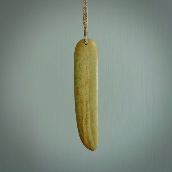 Raukaraka Pounamu drop pendant. Hand carved by Rhys Hall for NZ Pacific. Handmade jewellery for sale online. The cord is a 4-braid plait in tan and has a loop and pebble toggle closure. Drop necklace for men and women. Scandinesian Toki necklace hand made from New Zealand Jade.