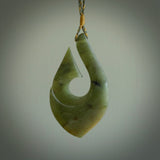 A hand carved hook design pendant, carved in New Zealand Jade. The colour is a beautiful green. The cord is green and tan and is length adjustable. Hand made by Rueben Tipene. Delivered with Express courier in a woven kete pouch.
