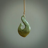 This picture shows a jade hook pendant, also called a hei-matau, carved for us in New Zealand jade. The jade is a wonderful deep mint green pounamu. This is a rare jade loved and valued for its distinctive colour. The carver is Ric Moor - and this is a beautiful example of his work. The cord is a four-plait, adjustable brown coloured necklace.