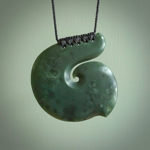 This picture shows a hand carved, large, jade koru pendant. It is a deep green colour and is a wonderful, large sized piece of jewellery. The cord is a four plait beige colour and adjustable so that you can position the pendant where it suits you best. This koru was carved for us by Ric Moor. Delivery is free worldwide.