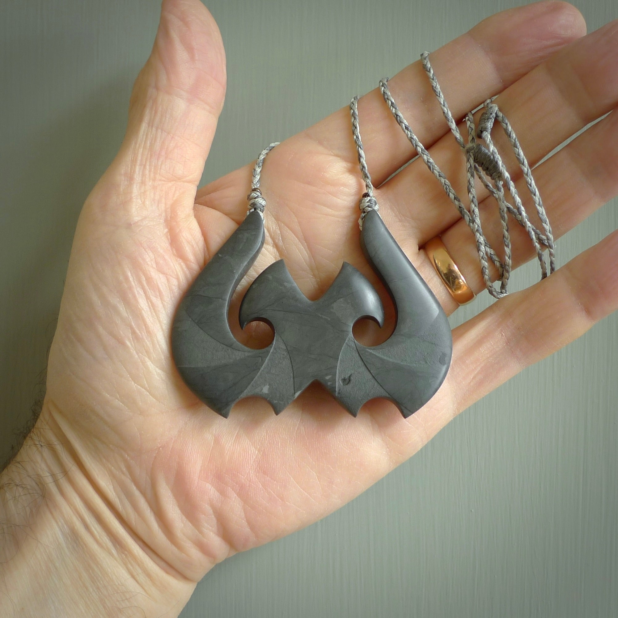 A hand carved large New Zealand Argillite double Hook, Matau, necklace. The cord is a black colour and is adjustable in length. A large sized hand made double hook necklace by New Zealand artist Rueben Tipene. One off work of art to wear.