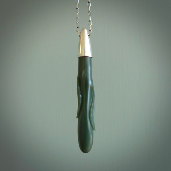 This picture shows a hand carved Inanga Pounamu, jade drop pendant with sterling silver cap and chain. The jade is a very dark green with a shimmer of light blue tones in the stone. It is suspended from a sterling silver clasp and we supply a sterling silver chain. Delivery is free worldwide.