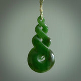 Ross Crump triple twist with koru pendant. Hand carved from rare New Zealand jade this is a beautiful pounamu pendant. The cord is hand plaited in green and white colours and is length adjustable. It has a floret in white. It is a delicate and very beautiful greenstone pendant. For sale online by NZ Pacific.