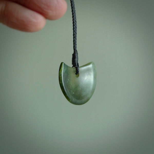 This piece is a small oval round, disc pendant. It was carved for us by Ric Moor from a lovely light and milky green piece of New Zealand jade that is semi-translucent when held to light. It is suspended on a black coloured braided cord that is length adjustable.