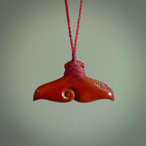 Hand carved, stained bone whale tail pendant. Carved for NZ Pacific bu Yuri Terenyi. Handmade jewellery for sale online. This is a beautiful bright reddish brown and is decorated with a koru at its heart and relief down one side. The cord is adjustable which allows you to position the pendant where it suits you best.