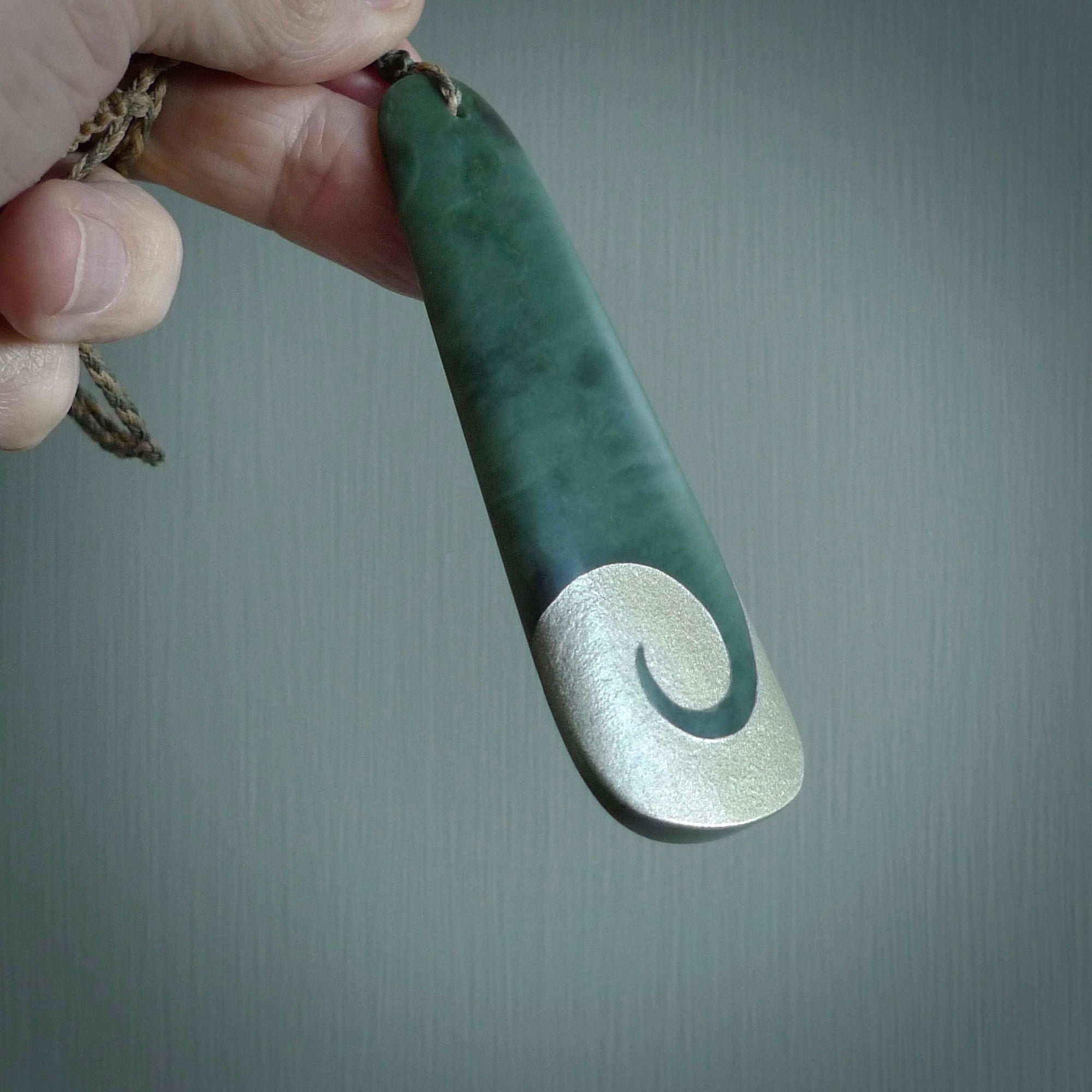 This photo shows a large jade drop shaped pendant. It a a lovely, colourful Inanga jade. The cord is a four plait green and tan colour and is adjustable in length. One only large, contemporary drop necklace from Jade, by Rueben Tipene.