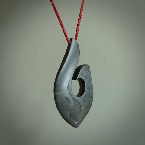 A hand carved large New Zealand Jade Hook, Matau, necklace. The cord is a Passion and Juicy Red colour and is length adjustable. A large sized hand made hook necklace by New Zealand artist Rueben Tipene. One off work of art to wear.