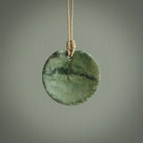 This piece is a oval round, disc pendant. It was carved for us by Ric Moor from a lovely light and milky green piece of New Zealand jade. It is suspended on a beige coloured braided cord that is length adjustable.