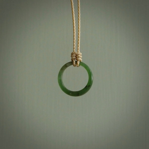 This piece is a oval round, ring pendant. It was carved for us by Ric Moor from a lovely light and milky green piece of New Zealand jade. It is suspended on a beige coloured braided cord that is length adjustable.