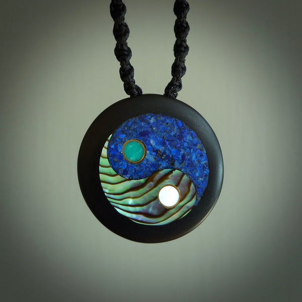 This photo shows a medium sized yin and yang pendant hand carved from horn with Mother of Pearl, Lapis Lazuli and Paua Shell inlay and brass. This is a stand out one off necklace for those who appreciate art to wear. It is provided with a cord in black that is a fixed length with Paua Shell Toggle. We ship this piece worldwide and shipping is included in the price.