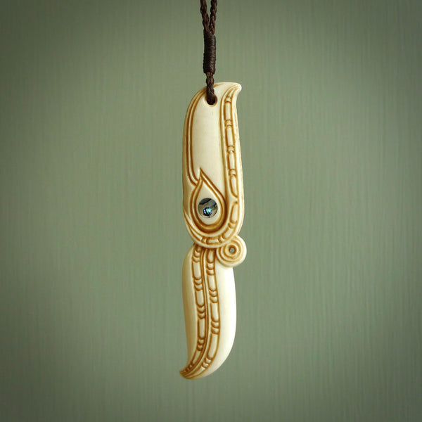This picture shows a carved hawk in bone. It is a drop shaped pendant. The artist has carved traditional decorative kowhaiwhai designs into the body and these run up the sides of the hawk. These have specific meanings. It is provided with a hand-plaited brown cord that is length adjustable. Shipping is included and we ship worldwide.