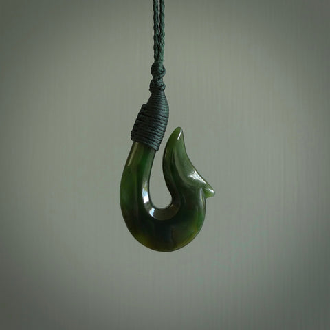 This photo shows a greenstone hook, or matau, pendant. It is a beautiful green British Columbia jade stone. The plaited cord is a manuka green colour. It is plaited and the length can be adjusted.
