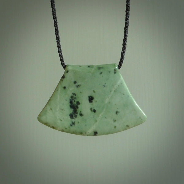 This picture shows a hand carved jade contemporary half-shield pendant. It is a mint green colour. This is a wonderful piece of jewellery. The cord is hand plaited and adjustable so that you can position the pendant where it suits you best. This piece was carved for us by Ric Moor. Delivery is free worldwide.