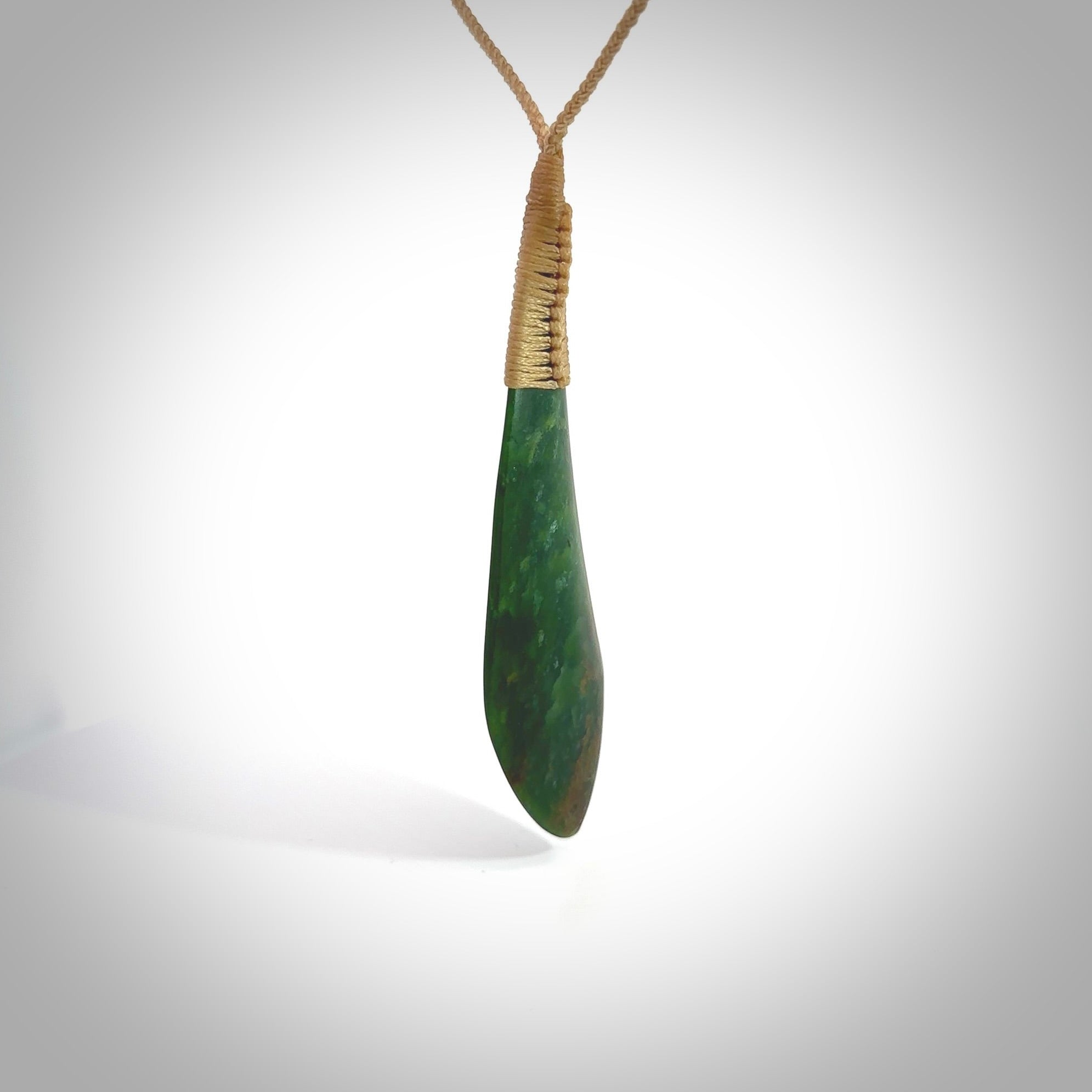 This photo shows a beautiful large jade drop. It is handcarved from a piece of green New Zealand pounamu, with fascinating light green inclusions throughout the stone. We have this on a creme coloured, adjustable four plait cord. We ship this worldwide with an express courier service. Postage is free.