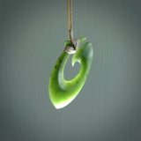 This picture shows a jade hook pendant, also called a hei-matau, carved for us in New Zealand jade. The jade is a wonderful deep mint green pounamu. This is a rare jade loved and valued for its distinctive colour. The carver is Ric Moor - and this is a beautiful example of his work. The cord is a four-plait, adjustable beige coloured necklace.