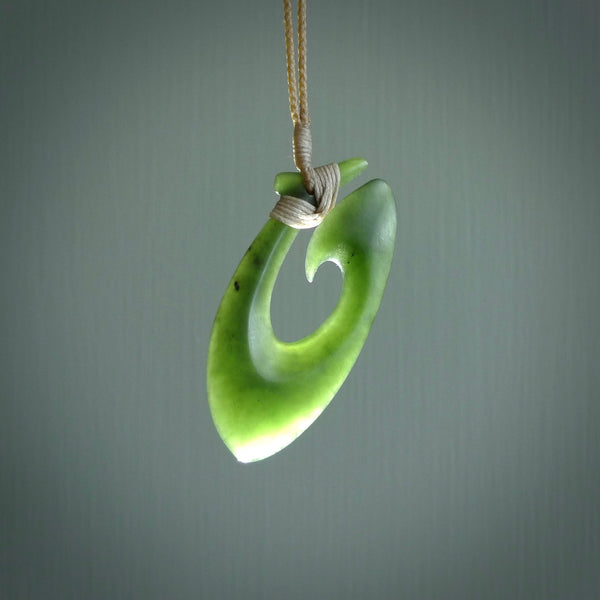 This picture shows a jade hook pendant, also called a hei-matau, carved for us in New Zealand jade. The jade is a wonderful deep mint green pounamu. This is a rare jade loved and valued for its distinctive colour. The carver is Ric Moor - and this is a beautiful example of his work. The cord is a four-plait, adjustable beige coloured necklace.