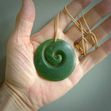 This picture shows a hand carved jade koru pendant. It is a deep green with orange colour and is a wonderful, large sized piece of jewellery. The cord is a four plait beige colour and adjustable so that you can position the pendant where it suits you best. This koru was carved for us by Ric Moor. Delivery is free worldwide.