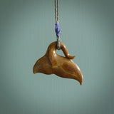 This picture shows a hand carved whale tail pendant. It is a dark, ginger brown colour and is handcarved from Woolly Mammoth tusk. The necklace is made from a braided cord in an olive green colour.