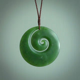 This picture shows a large hand carved jade koru pendant. It is a darker green colour which is quite translucent where the jade is thin. Although a large piece, it is a wonderful, delicate piece of jewellery. The cord is hand plaited and adjustable so that you can position the pendant where it suits you best. This koru was carved for us by Ric Moor. Delivery is free worldwide.