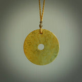 This picture shows a hand carved disc pendant made from a bright orange and green coloured flower jade. The front face is a unique design and the back is flat. It is provided with an adjustable kowhai yellow cord.