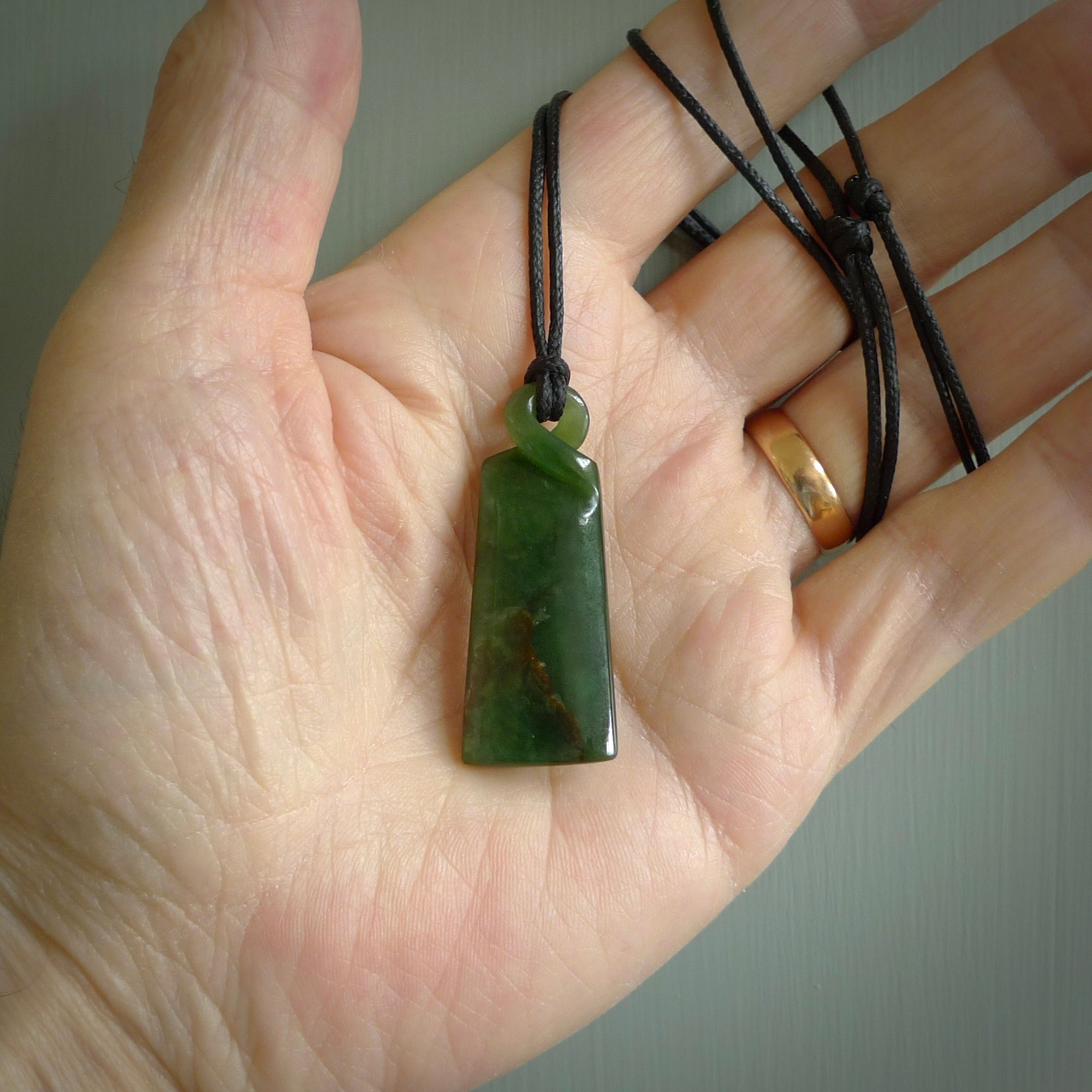 This pendant is a New Zealand jade single twist. It is hand carved from New Zealand Pounamu and has a mix of green, mint and pale colours interspersed throughout the stone. It has a fine twist, small and light. The cord is hand plaited and can be adjusted.