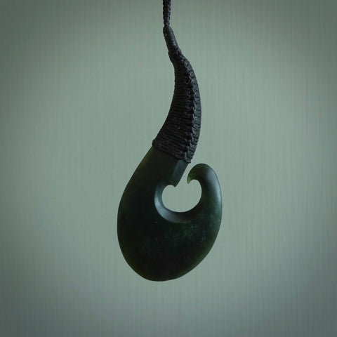 This picture shows a large deep green large jade hook pendant, also called a hei-matau, carved for us in New Zealand jade. The carver is Donna Summers - and this is a beautiful example of his work. The cord is a four-plait, adjustable black coloured necklace. 