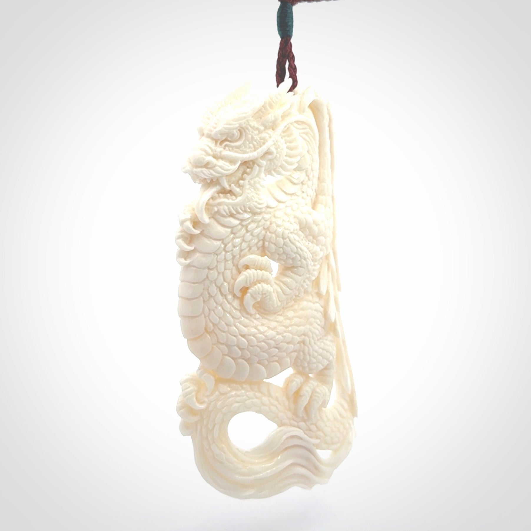 This is a hand carved bone dragon pendant. It is made from bone and has an adjustable Plum coloured cord. This is a large sized necklace and is a very unique, one only, pendant that is a piece for art lovers.