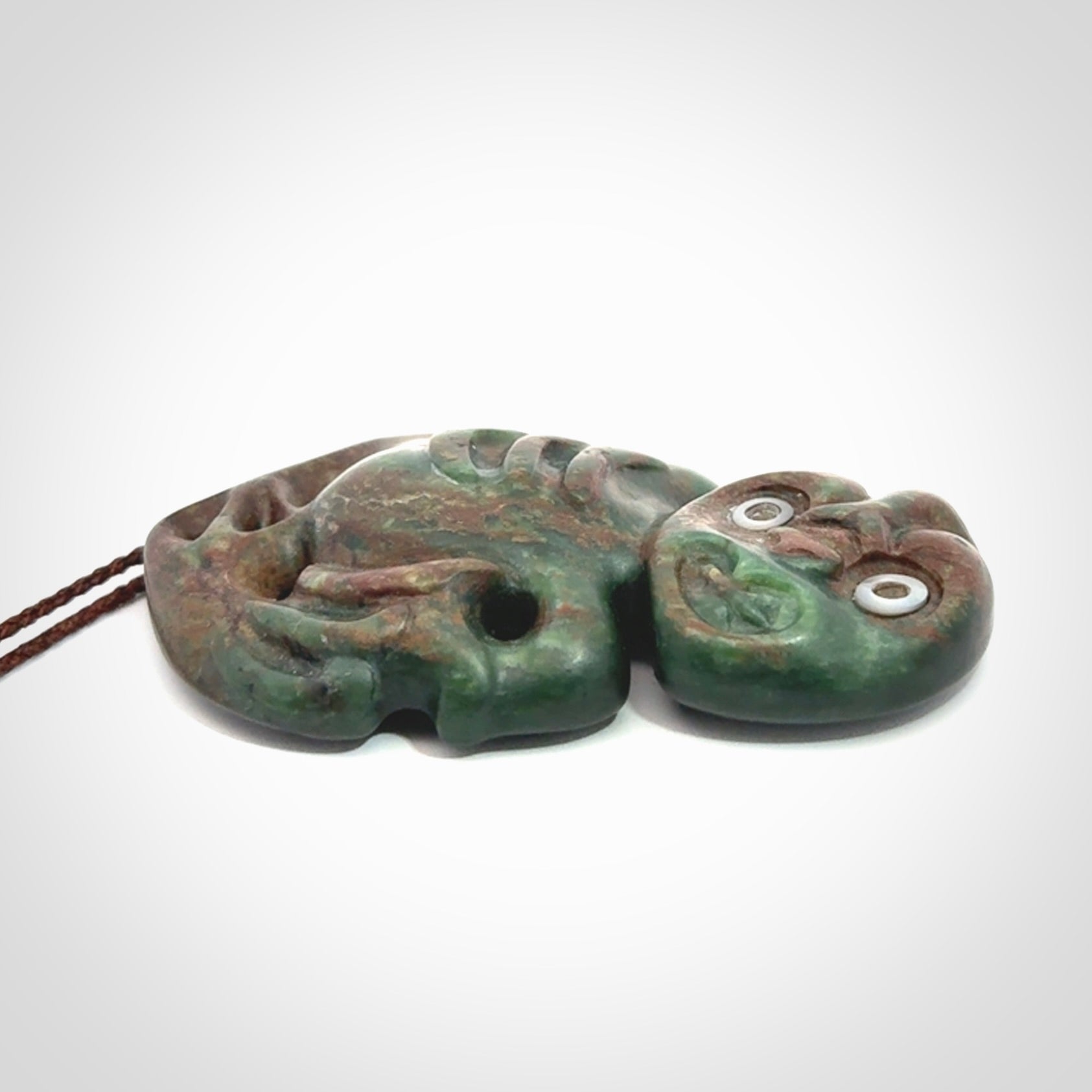 This is a large sized tiki - carved from gorgeous Marsden jade with Pāua Shell eyes. The craftsmanship is superb, this piece is as well carved as any we have seen. We have plaited an adjustable brown cord for this piece.&nbsp;