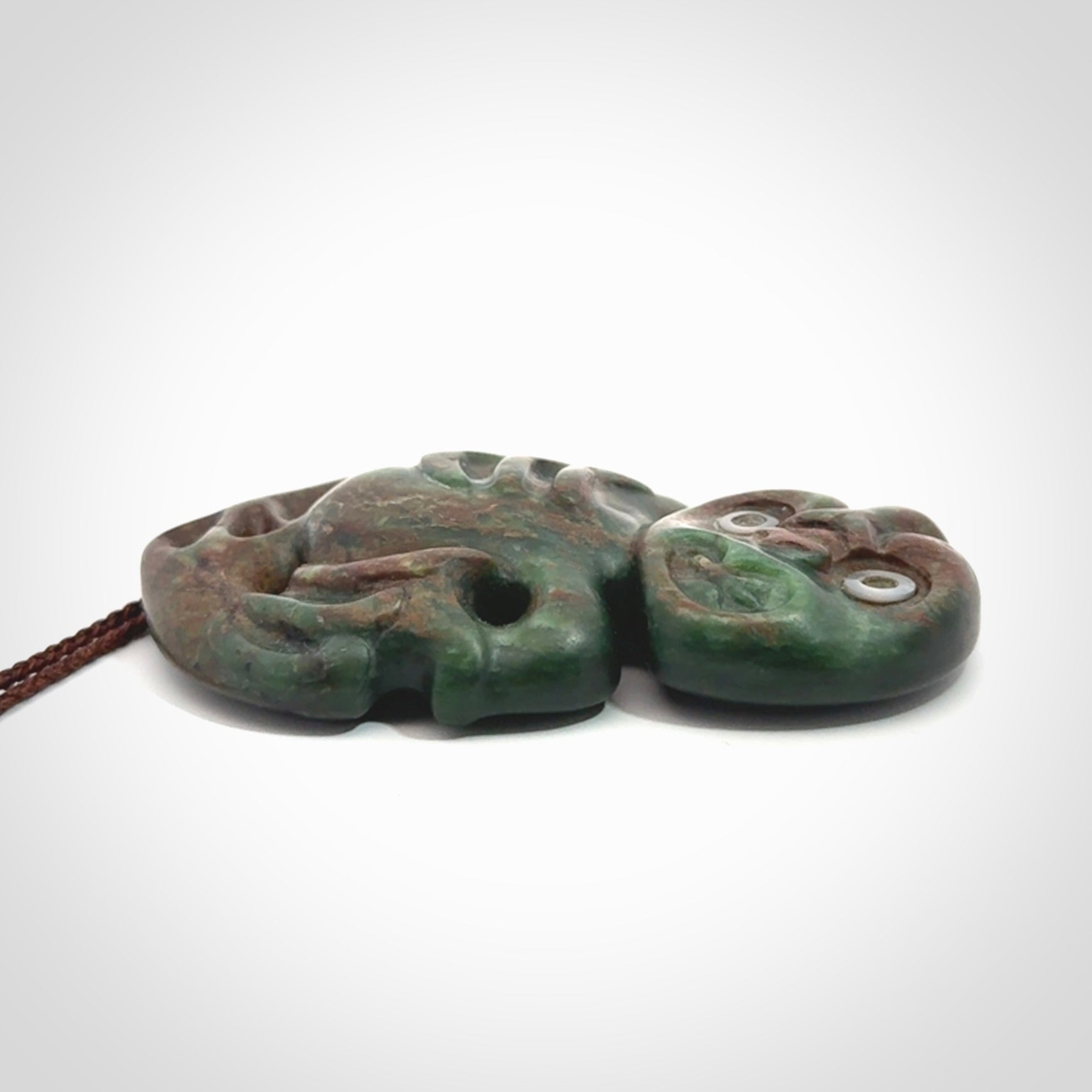 This is a large sized tiki - carved from gorgeous Marsden jade with Pāua Shell eyes. The craftsmanship is superb, this piece is as well carved as any we have seen. We have plaited an adjustable brown cord for this piece.&nbsp;
