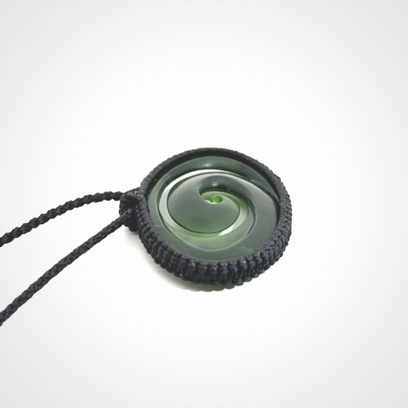 This picture shows a medium sized hand carved jade koru pendant. It is a darker green colour which is quite translucent where the jade is thin. The cord is bound in a macrame style and is adjustable so that you can position the pendant where it suits you best.