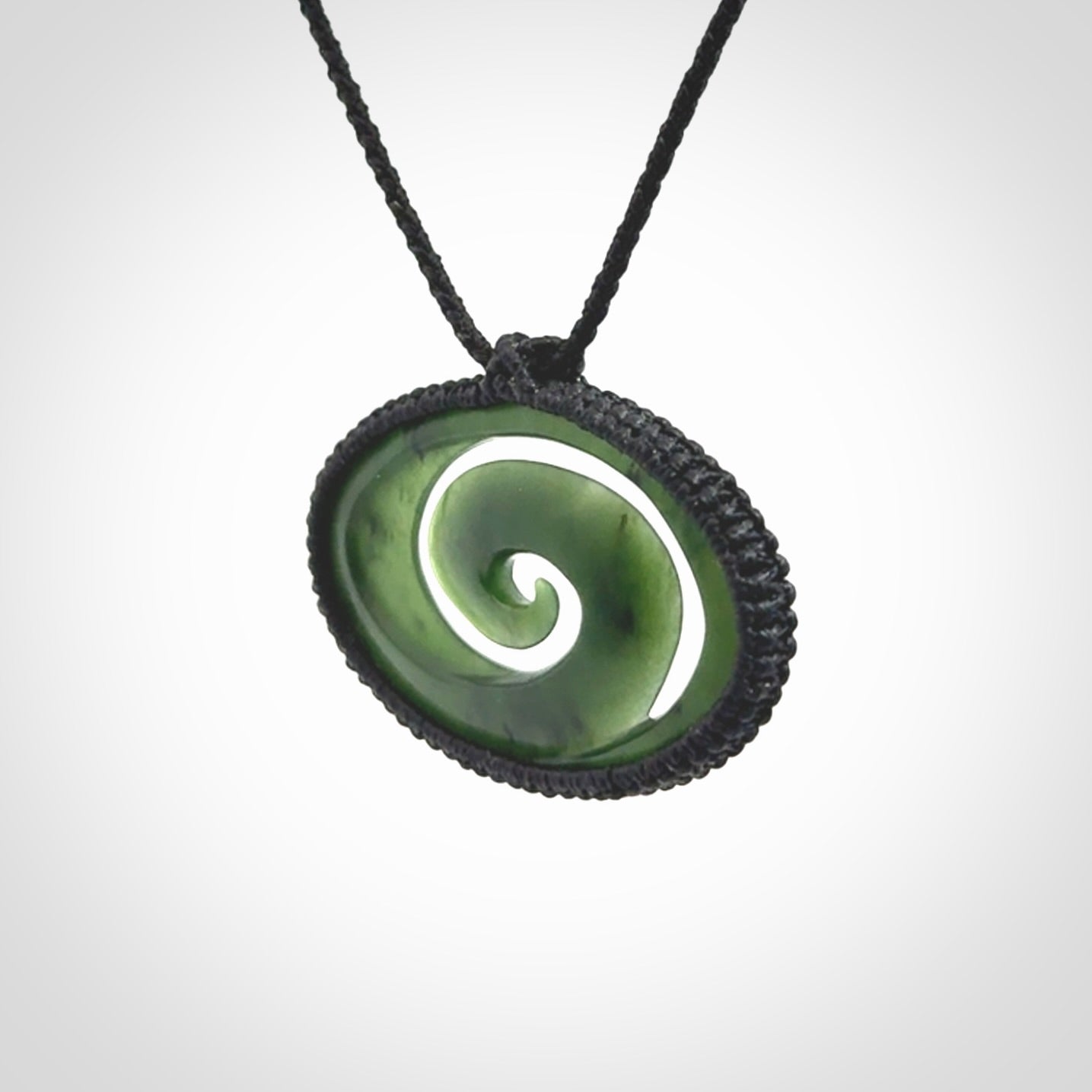 This picture shows a medium sized hand carved jade koru pendant. It is a darker green colour which is quite translucent where the jade is thin. The cord is bound in a macrame style and is adjustable so that you can position the pendant where it suits you best.